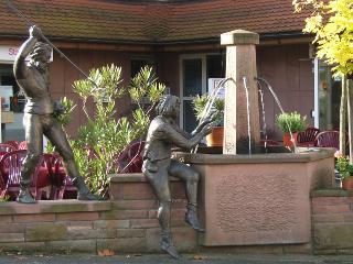 Motief aus dem Nibelungenlied: Siegfried und Hagen am Siegfriedbrunnen. Der Brunnen vor der Eisdiele im Ortsteil Wahlen. In diesem Haus sind auch unsere Wohnung 11 und 12.